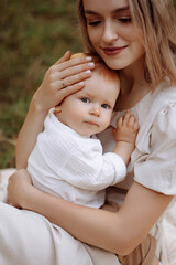 Woman sitting on the grass with a child in her arms. Relaxation or picnic in a summer park. Mother and child concept.