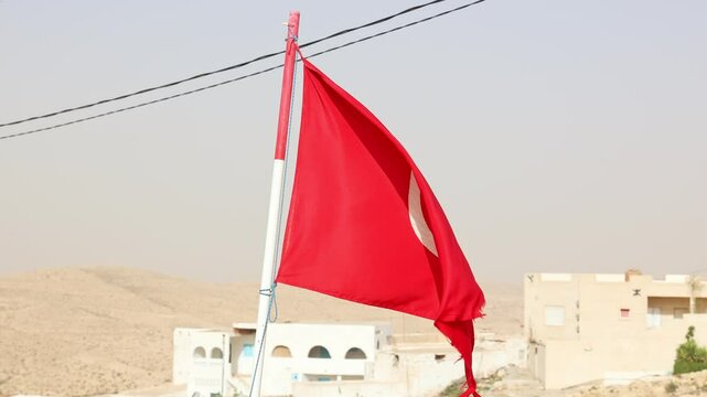 Tunisian flag is installed at highest point of impregnable fortress. Battered canvas of flag of Islamic country of Tunisia develops against background of blue sky