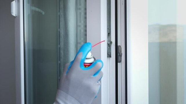 A man processes a door mechanism of metal-plastic constructions. Using a lubricating aerosol to reduce friction.