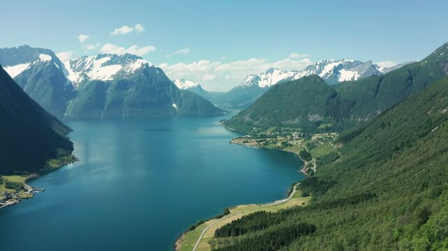 Aerial view of a deep fjord in Norway, surrounded by steep cliffs and green mountains under a clear sky.