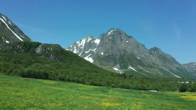 Aerial view of vast open valleys and distant mountain peaks in Norway, with a bright sky overhead as road winds along water's edge