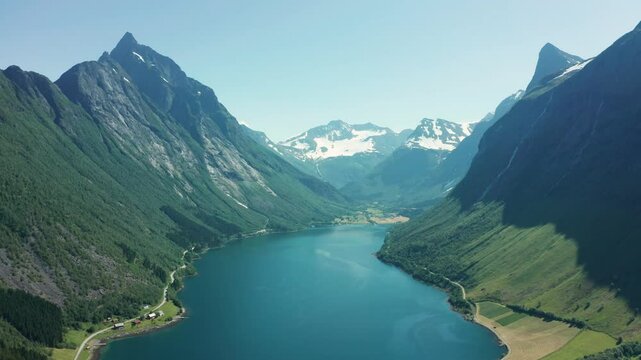 Panoramic aerial view of a deep blue fjord surrounded by towering mountains and green valleys in Norway.