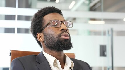 African American male professional sitting in modern office chair, eyes closed, wearing glasses and suit. Cconcept of mindfulness, relaxation, and stress relief in workplace, tranquility indoors