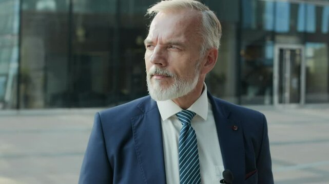 Tilt up shot of mid-aged Caucasian male news reporter wearing blue suit, white shirt and blue striped tie preparing for interview or formal recording, being set up with small lapel microphone