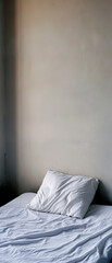 Cozy bed with rumpled sheets and soft pillow against a minimalistic wall, perfect for capturing comfort and relaxation.