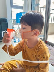 a child is using compressor nebulizer to nebulize his respiratory while heavy nose due to cold. pediatric home care for child with running nose and cough. toddler using nebulizer in viral infection 