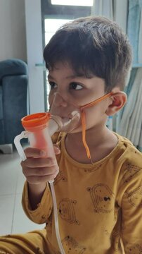 a child is using compressor nebulizer to nebulize his respiratory while heavy nose due to cold. pediatric home care for child with running nose and cough. toddler using nebulizer in viral infection 