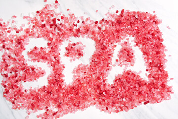 Red salt crystals are scattered on a white marble surface as a SPA word. The salt crystals are a beautiful pink color and have a natural, earthy feel