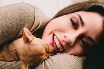 Happy young woman lying and playing with her puppy dog on a couc