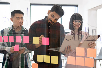 Creative team collaborating in modern office environment, working on project ideas using colorful sticky notes and laptop. Concept of teamwork, brainstorming, and innovation.