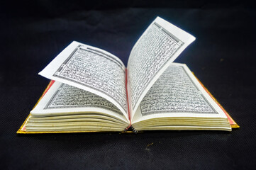 Open Quran book with intricate Arabic script on black background, highlighting the sacred text of...