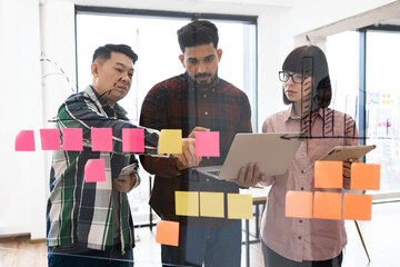 Team collaborating on project using sticky notes and laptops in modern office. Brainstorming session for creative ideas and project planning. Diverse group focused on teamwork and innovation.