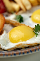 Breakfast plate with fried eggs, sausage, tomatoes, and fries served on a decorative blue plate