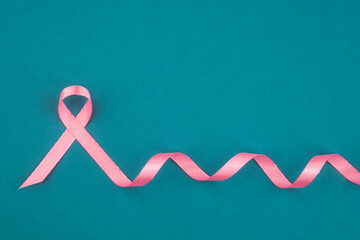 Pink ribbon symbolizing breast cancer awareness on teal background with ribbon curls