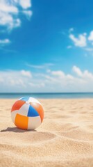 Obraz premium A vibrant beach ball resting on golden sand, with a clear blue sky and ocean in the background, perfect for summer vibes.