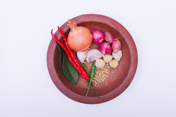 onion, vibrant chili, peppers, and whole candlenuts artistically arranged on a brown plate....