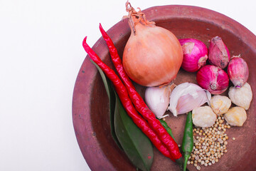 onion, vibrant chili, peppers, and whole candlenuts artistically arranged on a brown plate....