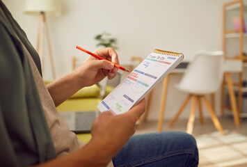 Man sitting on sofa at home or at office with pen in hand planning tasks and to do list in his notepad. Man looking at plan schedule with daily appointment. Time management and planner concept.