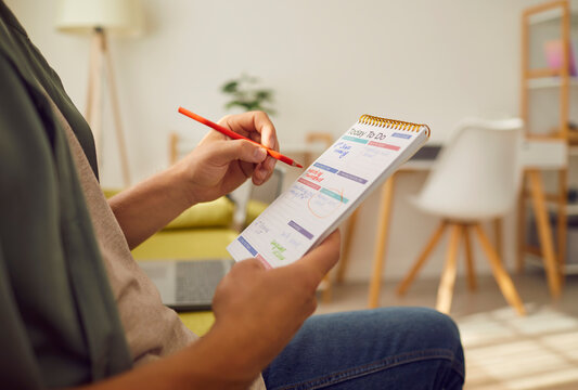 Man sitting on sofa at home or at office with pen in hand planning tasks and to do list in his notepad. Man looking at plan schedule with daily appointment. Time management and planner concept.