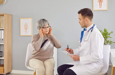 Portrait of sick stressed senior woman sitting at doctor's office suffering from headache or having...