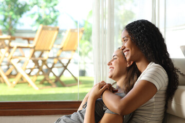 Happy lesbian couple looking through a window at home