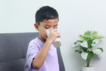 Asian little cute boy drinking milk. stays home with a smiling face, feels happy, and enjoys...