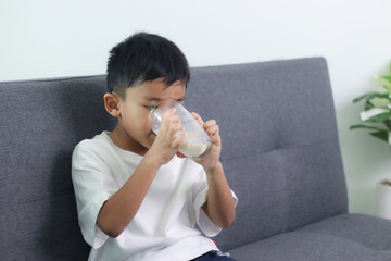 Asian little cute boy drinking milk. stays home with a smiling face, feels happy, and enjoys...