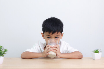 Asian little cute boy drinking milk. stays home with a smiling face, feels happy, and enjoys...