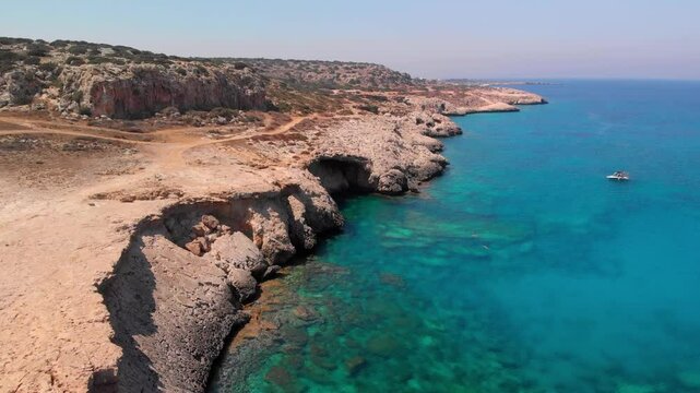 Low angle shot of Cape Greco cliffs standing against the bright blue Mediterranean Sea in Cyprus.