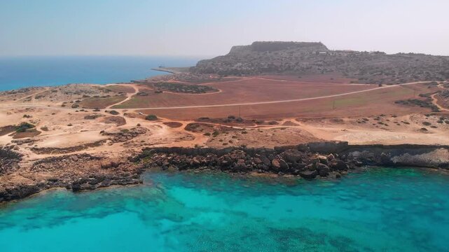 Aerial footage of Cape Greco, highlighting the blue sea against the dry, brown terrain.