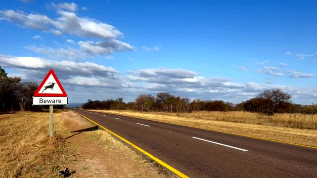Beware road sign next to highway warning motorists against crossing game animals