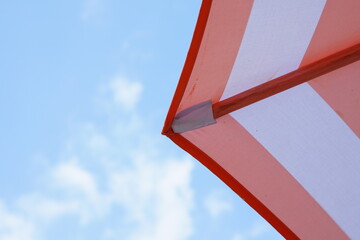 A low-angle view where a striped beach parasol with a wooden frame has been opened to provide shade from the sun against a blue sky. Summer vacation concept