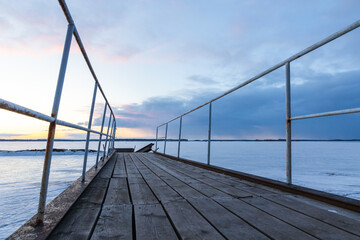 Obraz premium Frozen pier is under sunset sky in the evening, perspective view
