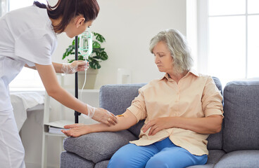 Young friendly nurse or caregiver help sick senior elderly woman patient in receiving IV drip...