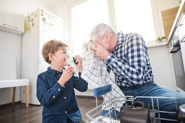 Boy helping grandfather clean the kitchen, unloading clean dishes out of the dishwasher....