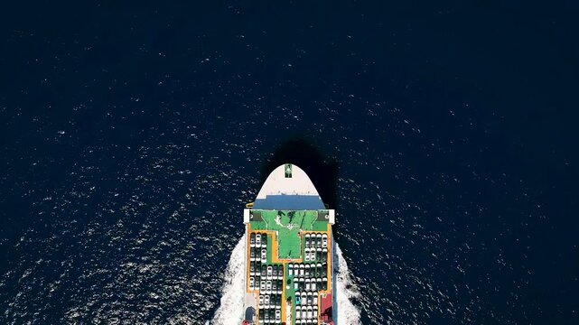 Aerial top down view of a large, industrial car carrier transport ship cruising with speed over the ocean