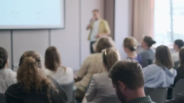 Group of people attentively listening to a speaker during a business seminar in a modern conference room.