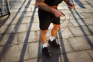 Cropped shot of tattooed sportsman holding skipping rope outdoors