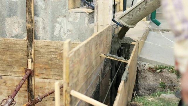 Construction Workers Pouring Cement into New Building Foundation