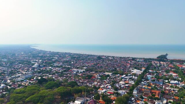 Drone shot of Tuban Regency in East Java, Indonesia, highlighting the cityscape with its blend of urban and natural landscapes and beach. The Java Sea is in the background.