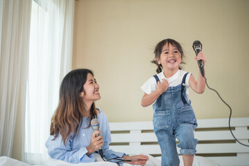 Happy Asian family loving children, kid and her sister holding microphone and singing together on bed in bedroom