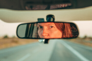 Naklejka premium Returning from weekend vacation. Eyes and face female driver are reflected in car rearview mirror