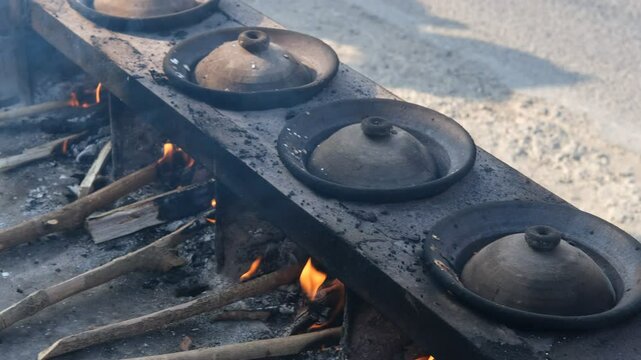 Traditional serabi clay pot cooking on a rustic outdoor stove, fueled by wood fire. The scene captures the essence of local cuisine preparation with earthy tones and an authentic rural setting.
