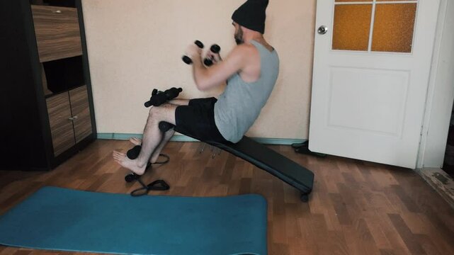 An adult man in a room is doing sports lying on a gym bench, training his abdominal muscles