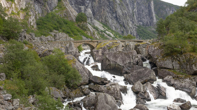 Old stone bridge over a white foaming river. The bridge is ancient engineering. It is now closed to traffic due to the risk of landslides