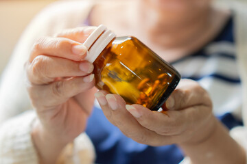 An elderly woman is sitting at a table and holding the bottle of pills in her hands.