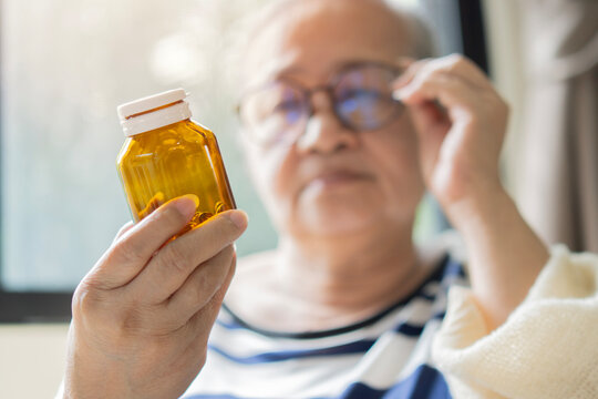 Concerned senior woman adjusting her eyeglasses for looking the a bottle of medicine