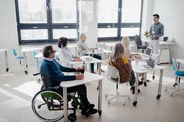 Teacher explaining senior students how to work with laptop and internet. Elderly people attending computer and technology education class. Digital literacy.