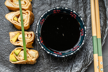 Tamagoyaki or traditional Japanese omelette with avocado and cheese on a black mica plate with soy sauce and chopsticks. Top view. Close-up. High quality photo