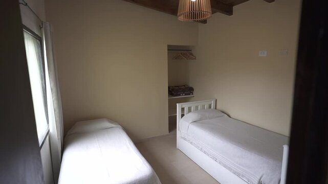 Small compact bedroom featuring two twin beds, minimalist decor, and natural light streaming through a window, creating a serene and inviting atmosphere